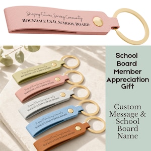 May include: A collection of keychains in various colors, including pink, green, white, blue, and brown. Each keychain features a gold-colored ring and a strap with the text "Shaping Futures, Serving Community ROCKDALE I.S.D. SCHOOL BOARD."