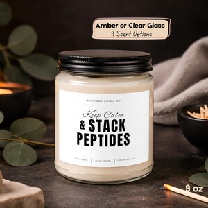 May include: A clear glass candle jar with a black lid and a white label reading Wildwood Candle Co. Keep Calm & STACK PEPTIDES. The label includes 9 oz / 245g, 50-60 hours, and 100% natural soy. A text box above states Amber or Clear Glass 9 Scent Options.