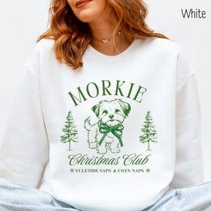 May include: White sweatshirt with a green graphic featuring the word "Morkie" above a dog illustration wearing a green bow. The text "Christmas Club" and "Yuletide Yaps & Cozy Naps" are also included in the design.