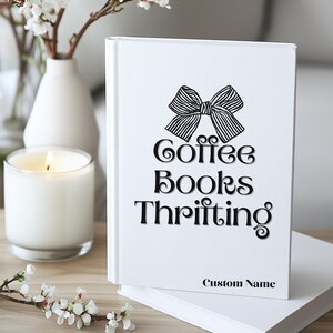 K&ouml;nnte beinhalten: Ein wei&szlig;es Buch mit einer schwarzen Schleifengrafik und den Worten "Coffee Books Thrifting". Das Buch hat den Text "Custom Name" unten. Eine brennende Kerze und eine Vase mit Blumen sind im Hintergrund.