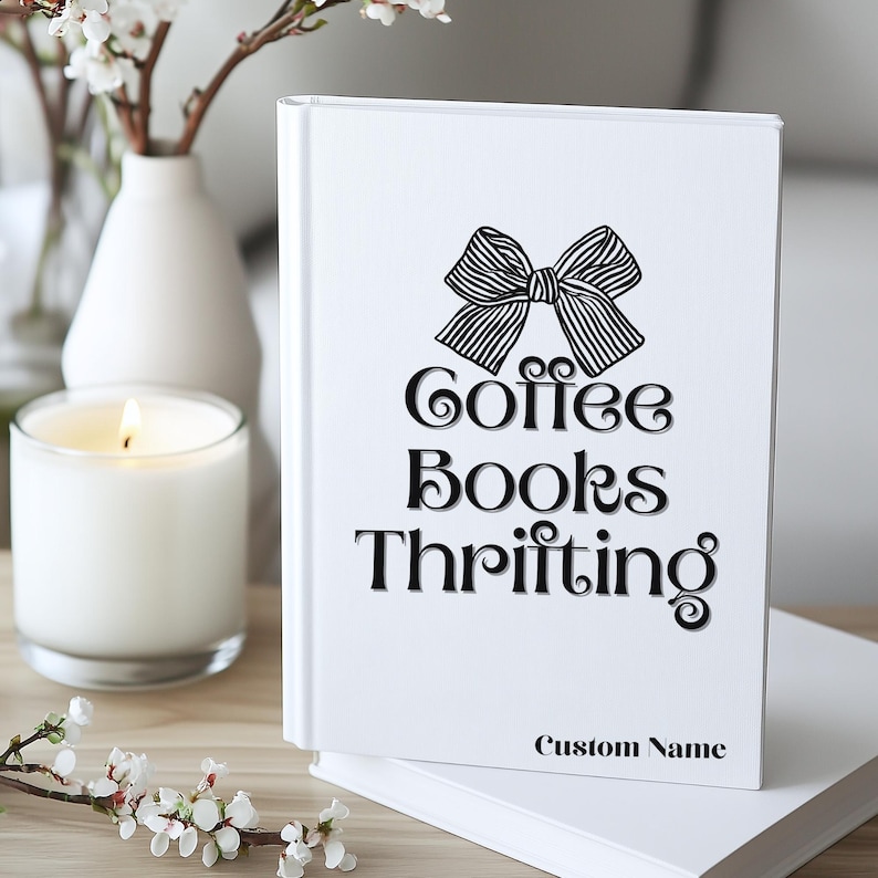 K&ouml;nnte beinhalten: Ein wei&szlig;es Buch mit einer schwarzen Schleifengrafik und den Worten "Coffee Books Thrifting". Das Buch hat den Text "Custom Name" unten. Eine brennende Kerze und eine Vase mit Blumen sind im Hintergrund.