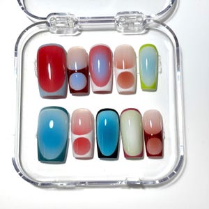 Puede incluir: Un juego de diez uñas postizas en una caja de plástico transparente. Cada uña presenta un diseño único con un degradado de colores, incluyendo rojo, azul, rosa y verde. Algunas uñas tienen un acento circular.