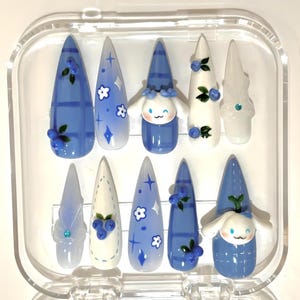 以下が含まれることがあります： 透明なプラスチックケースに入った10本のつけ爪のセット。爪には、青い格子柄、白と青のグラデーション、花のアクセント、漫画のキャラクターなど、さまざまなデザインが施されています。一部の爪には、3Dのブルーベリーの装飾が施されています。