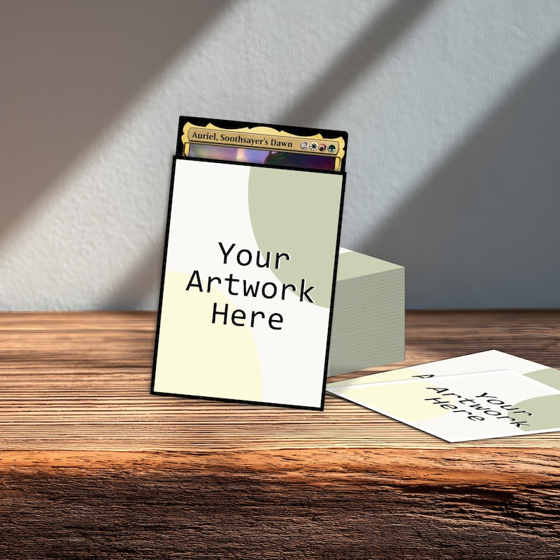 May include: A white card sleeve with the text "Your Artwork Here" and a black border, holding a Magic: The Gathering card. A stack of similar sleeves and a loose sleeve are on a wooden surface.
