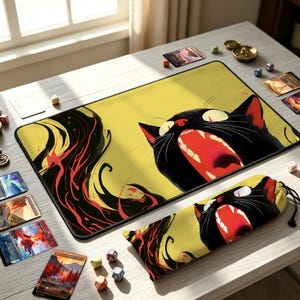 May include: A rectangular playmat and a matching drawstring bag featuring a graphic illustration of a black cat with a wide-open mouth, yellow eyes, and flowing red and black abstract shapes against a pale yellow background.