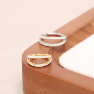 May include: Two double-band rings with an opal-like appearance. One ring has a gold band, and the other has a silver band. The rings are displayed on a brown wooden tray with a white cloth.