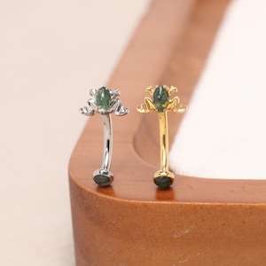 May include: Two curved barbell body jewelry pieces, one in silver-tone and one in gold-tone metal. Each features a frog-shaped top with a marquise-cut green moss agate stone set in the center and a matching round green moss agate stone at the base.