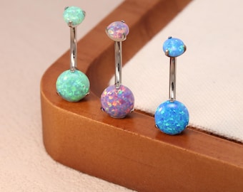 May include: Three belly button rings with opal-like spheres in shades of green, purple, and blue. Each ring has a silver-colored, curved barbell. The opal spheres have a textured, iridescent appearance.