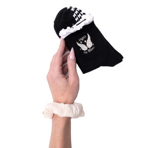 May include: Black socks with a white and black checkered pattern at the top and a white ruffled trim. The socks have an embroidered design of angel wings and the text "Angels Do Pilates".