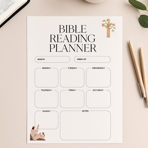 Könnte beinhalten: Ein weißer Bibel-Leserplaner mit einem Kreuz-Grafik und dem Text "BIBLE READING PLANNER". Der Planer enthält Abschnitte für den Monat, die Woche und tägliche Einträge. Eine Tasse Kaffee, Stifte und ein Buch sind ebenfalls sichtbar.
