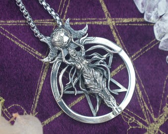 May include: A silver pendant necklace featuring a detailed figure within a pentagram. The pendant has intricate designs and is suspended from a chain. The background is a deep purple fabric with gold accents, and the necklace is displayed with crystals and dried flowers.