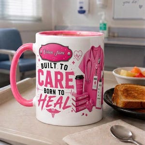 Peut inclure: Un mug en céramique blanc avec une anse et un intérieur roses, portant l'inscription "BUILT TO CARE BORN TO HEAL", une blouse médicale rose, une pile de livres marqués "COMPASSION", "DEDICATION", "STRENGTH", un symbole médical et un cœur.