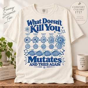 Op de afbeelding: Een off-white t-shirt met korte mouwen en een blauwe grafische print. Het ontwerp toont de tekst "What Doesn't Kill You Mutates And Tries Again" samen met illustraties van cellulaire mutatieniveaus, een DNA-streng en wetenschappelijke symbolen.