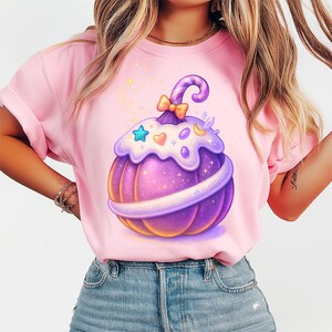Peut inclure: T-shirt rose avec un motif de citrouille violette. La citrouille a un glaçage blanc sur le dessus, une tige en spirale et un nœud. Elle est décorée d'étoiles, de cœurs et de lunes. La citrouille a une texture scintillante. Le t-shirt est en matière douce.