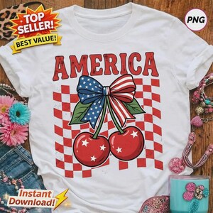 Peut inclure: Un t-shirt blanc avec un motif rouge, blanc et bleu représentant deux cerises surmontées d'un nœud aux couleurs du drapeau américain. Le mot AMERICA est imprimé en rouge au-dessus des cerises sur un fond à carreaux rouges et blancs.