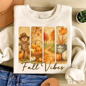 Peut inclure: Sweat-shirt crème avec un motif aquarelle représentant des éléments d'automne. Le motif comprend un épouvantail, des citrouilles dans un panier, un chemin à travers les arbres et une feuille. Les mots "Fall Vibes" sont écrits en écriture cursive.