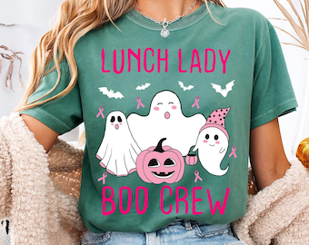 Może przedstawiać: Zielona koszulka z różowym napisem "LUNCH LADY BOO CREW". Koszulka przedstawia białe duszki, różową dynię, nietoperze i różowe wstążki. Projekt jest wyśrodkowany z przodu.