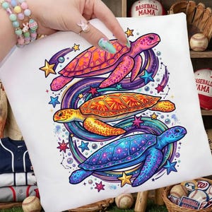 May include: White pillow with a colorful illustration of three turtles. The turtles are in shades of pink, orange, yellow, and blue, surrounded by stars and swirling lines. The design is vibrant and eye-catching.