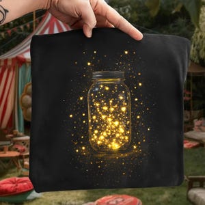 Peut inclure: Sac fourre-tout noir avec un motif de bocal Mason rempli de lumières dorées. Le bocal est au centre, entouré de particules scintillantes. Le design évoque un thème fantaisiste et magique.