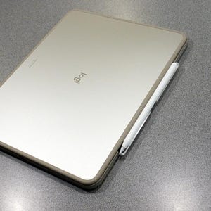 Op de afbeelding: Een zilveren tablet met het Logitech-logo en een witte stylus. De tablet is rechthoekig met afgeronde hoeken en een donkergrijze rand. De stylus is aan de zijkant van de tablet bevestigd. De achtergrond is een grijs oppervlak.