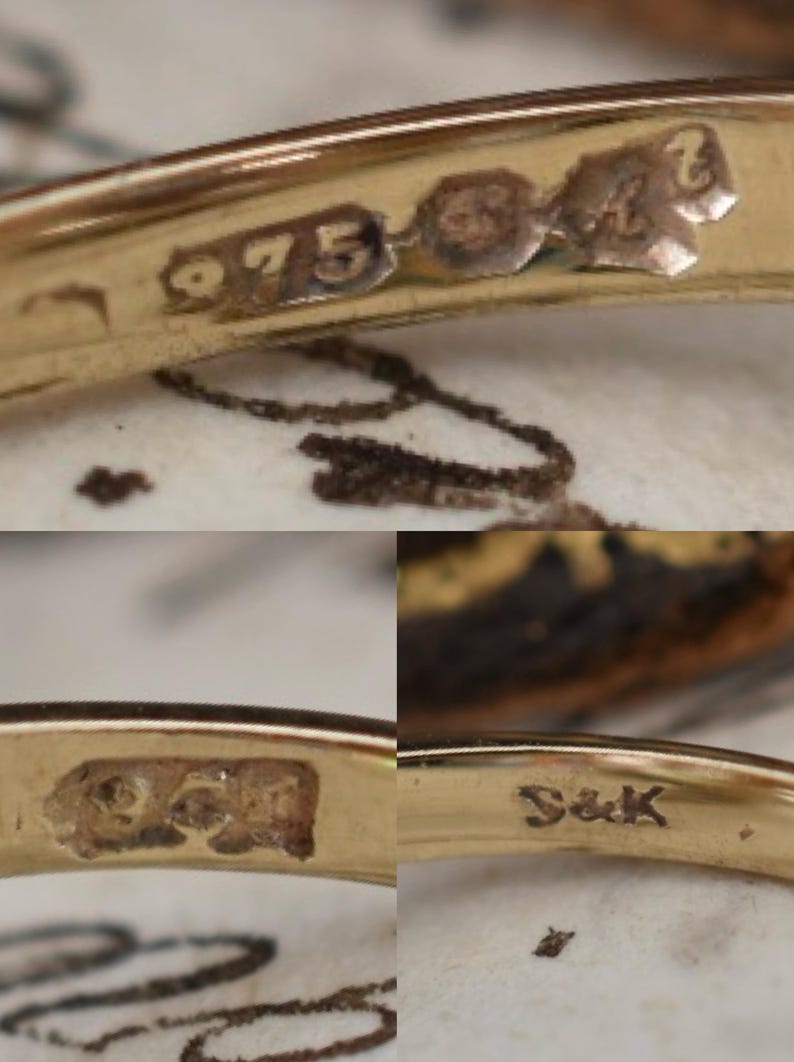 May include: Close-up of a gold ring with several hallmarks. The ring is stamped with "975" and other markings. The ring's surface is reflective, and the details are visible against a blurred background.