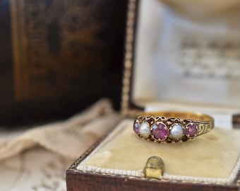 May include: A gold ring with five gemstones, alternating between pink and white. The ring is displayed in a vintage brown jewelry box with a cream-colored interior. The ring is likely antique or vintage.