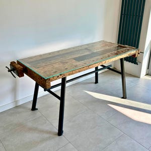 Peut inclure: Un établi rustique avec un plateau en verre et des pieds en métal noir. La base en bois a un étau à une extrémité. La table mesure environ 152 cm de long et 76 cm de large.