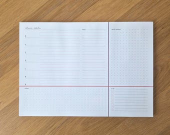 May include: A white planner with the text "Unsere Woche" at the top. The planner has sections for daily scheduling, a to-do list, and a calendar grid. A red line separates the sections. The planner is on a wooden surface.