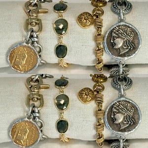 May include: An assortment of gold and silver bracelets. One bracelet features a gold coin pendant with a deer image, another has green gemstone accents, and others have decorative charms and coin-like pendants. The bracelets are displayed on a white surface.
