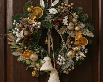 May include: A festive Christmas wreath with dried orange slices, gold ornaments, and white berries. Two cream-colored bell ornaments hang below the wreath. The wreath is displayed on a dark brown wooden door.