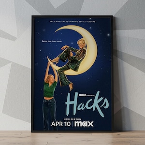 Puede incluir: Un póster enmarcado de la serie de televisión "Hacks" muestra a una mujer sentada en una luna creciente, con otra mujer debajo. El fondo es un cielo nocturno azul oscuro con estrellas. El texto incluye "Hacks", "New Season" y "Apr 10 max."