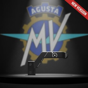 May include: Black metal motorcycle component with a speedometer graphic. The background displays the Agusta logo and the text "NEW VERSION" in red. The part is on a dark surface.