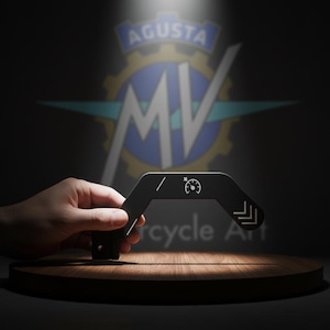 May include: A black motorcycle-themed decorative item with white graphic details, including a speedometer icon and directional arrows. The Agusta MV logo is visible in the background. The item is displayed on a wooden platform.