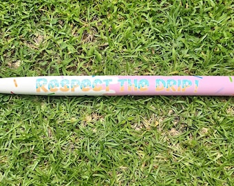 May include: A wooden baseball bat with a brown handle and a white and pink barrel. The barrel is decorated with the text "Respect the Drip" in colorful letters and sprinkles.