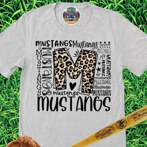 May include: A light gray t-shirt with the word "Mustangs" in various fonts and a leopard print "M". A baseball bat, baseball glove with a baseball, and black and gray athletic shoes are also in the image.