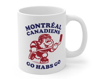 May include: White ceramic mug with the text "MONTREAL CANADIENS" and "GO HABS GO" in navy blue. A red cartoon hockey player with a hockey stick is depicted on the mug. The mug has a white handle.