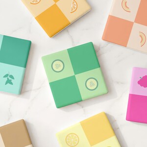 May include: A collection of square coasters featuring a checkerboard pattern in various colors. Each coaster displays a unique fruit or vegetable icon, including orange slices, cucumber rounds, and berries, rendered in a simple, flat graphic style.