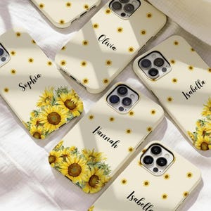 May include: Cream-coloured phone cases with sunflower designs. Some cases feature names like "Olivia", "Sophia", "Hannah", and "Isabella" in black script. The cases have a repeating pattern of small sunflowers and larger sunflower bouquets.