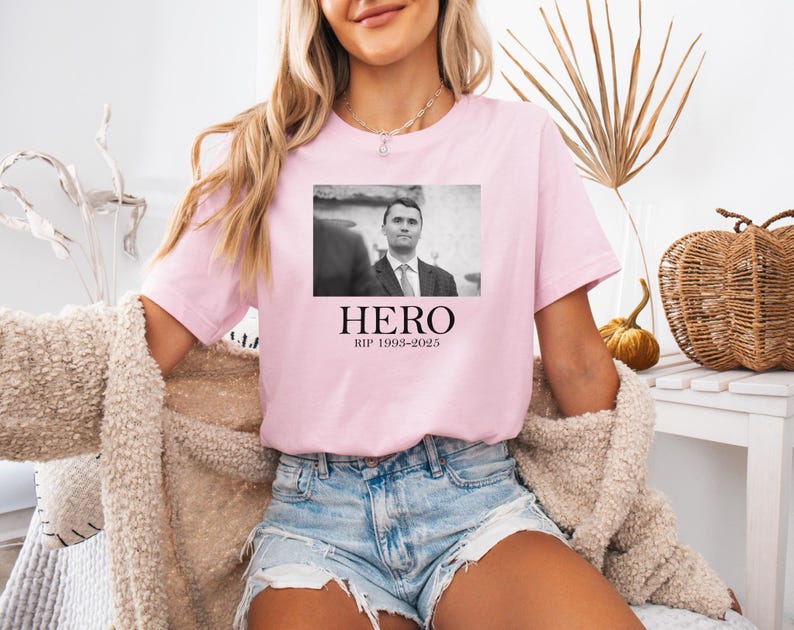 A woman wearing a pink t-shirt with a black and white photo of a man and the text "HERO RIP 1968-2005" printed on it.