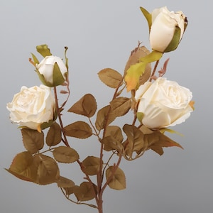 May include: A stem of artificial roses with four cream-coloured blooms and several buds. The faux flowers have brown stems and leaves with hints of yellow and green. The roses are in various stages of bloom, with some fully open and others still closed.
