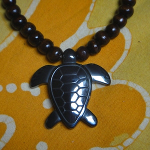 May include: A dark brown wooden beaded necklace with a black turtle pendant.