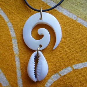 May include: White shell pendant necklace with a spiral design and a cowrie shell charm. The necklace is on a black cord.