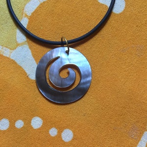May include: A black cord necklace with a silver and grey shell pendant featuring a carved spiral design.
