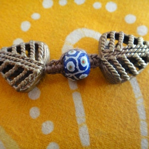 May include: A close-up of a necklace with two silver leaf-shaped charms and a blue and white glass bead in the center.