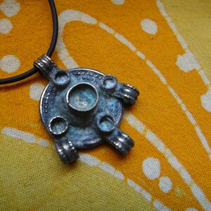 Puede incluir: Un colgante de plata con un diseño circular y cinco círculos más pequeños alrededor de un círculo central. El colgante está unido a un cordón negro.