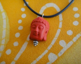 May include: A red Buddha pendant necklace with a silver chain. The pendant is a detailed sculpture of a Buddha's face.