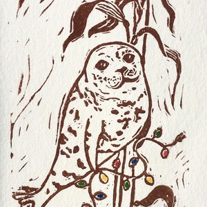 Puede incluir: Una impresi&oacute;n linograbada marr&oacute;n de un b&uacute;ho posado en una rama con luces de colores. El b&uacute;ho est&aacute; mirando directamente al espectador. La firma del artista, "Xena Battle", est&aacute; en la esquina inferior derecha.