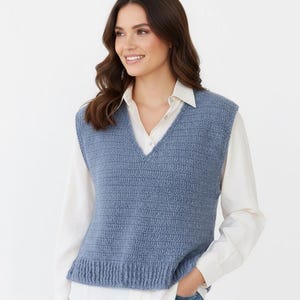 Puede incluir: Un chaleco de punto azul claro con cuello en V. El chaleco se lleva sobre una camisa blanca con cuello y vaqueros azules. El chaleco de punto tiene un dobladillo acanalado y un aspecto texturizado.