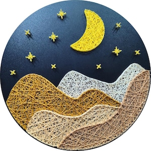 Peut inclure: Une œuvre d'art en fils tendus circulaire sur fond noir représentant un croissant de lune jaune et des étoiles au-dessus de chaînes de montagnes superposées. Les montagnes sont formées de fils entrecroisés jaune moutarde, blanc et beige.