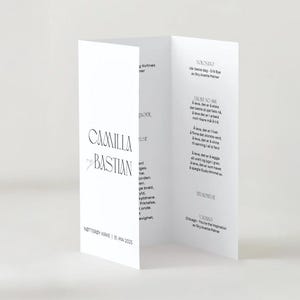 May include: A white, folded wedding program with black text. The names "Camilla Bastian" are displayed prominently. Additional text includes the wedding date and location. The program is open, revealing more text.